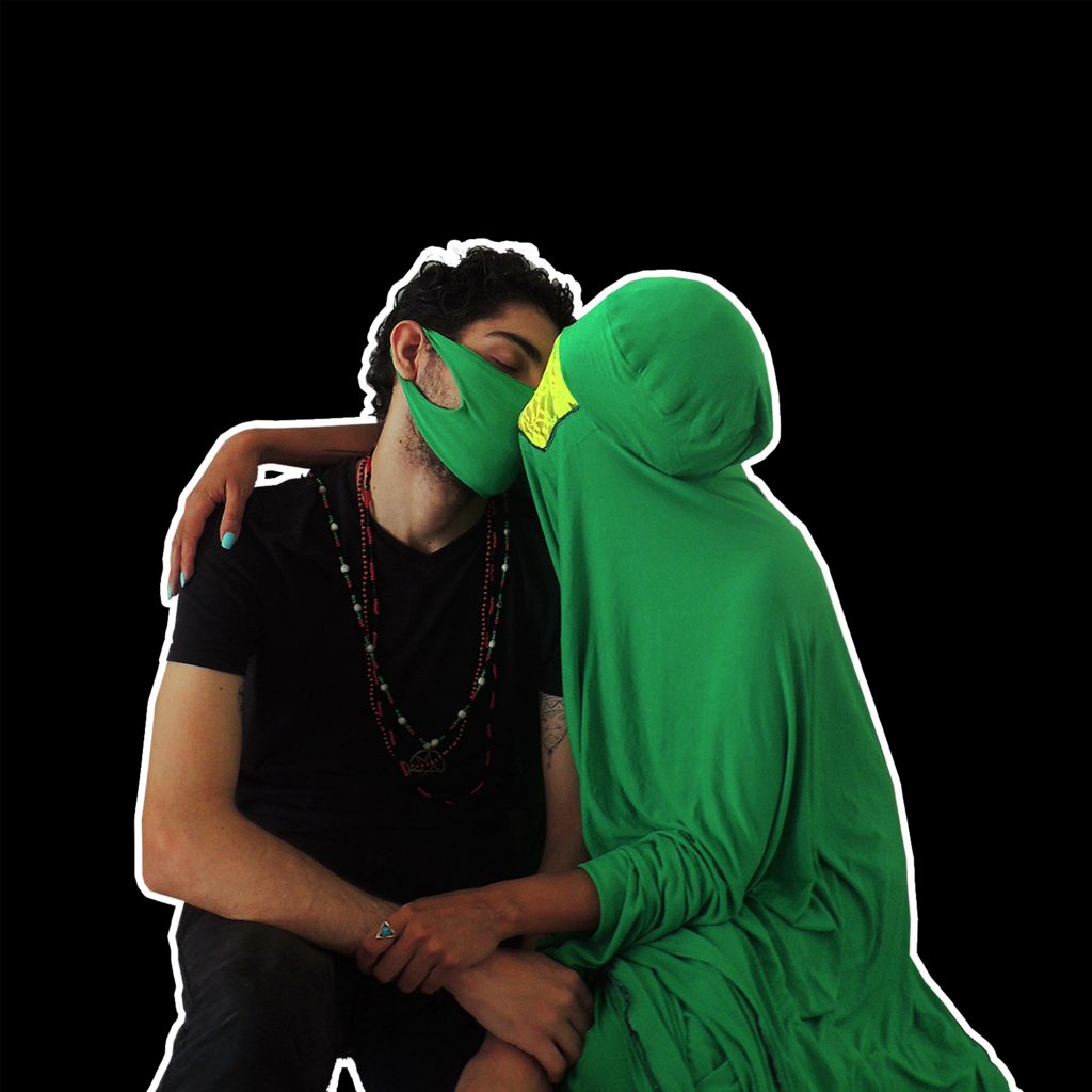 a woman dressed on an body covering green outfit is kissing a man wearing a green mask and dressed in black with some bead chains hanging from his neck.